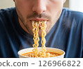 Close-up of a person slurping hot, steamy noodles directly from a bowl, showcasing the enjoyment of a quick and delicious meal. 126966822