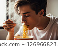 Close-up of a person slurping hot, steamy noodles directly from a bowl, showcasing the enjoyment of a quick and delicious meal. 126966823
