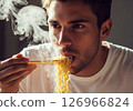 Close-up of a person slurping hot, steamy noodles directly from a bowl, showcasing the enjoyment of a quick and delicious meal. 126966824
