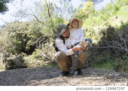 Father helping son taking off shoe while hiking in nature Father helping son taking off shoe while hiking in nature 126967297