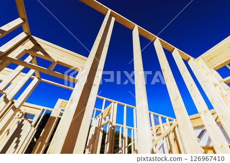 Wooden beams framework of building rise towards clear blue sky on ongoing construction. 126967410