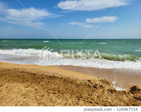 A stormy sea with white foam and a beach on a clear sunny day. The concept of recreation. A stormy sea with white foam and a beach on a clear sunny day. The concept of recreation. 126967534