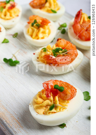 Boiled eggs stuffed with yolk and seasoned with mayonnaise, stuffed eggs with shrimp, on a white wooden chopping board, selective focus, close-up, without people, 126968433