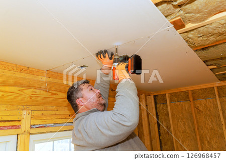 Homeowner works on attaching drywall to ceiling in basement renovation project during home renovation. 126968457