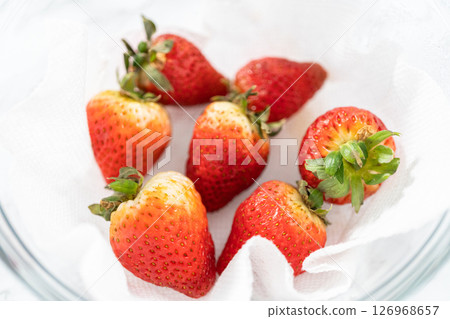 Bright red strawberries, interspersed with signs of mold, rest in a glass bowl lined with a paper towel on a white napkin, indicating improper storage techniques. Bright red strawberries, interspersed with signs of mold, rest in a glass bowl lined with a paper towel on a white napkin, indicating improper storage techniques. 126968657