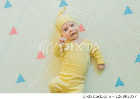 Adorable baby in a yellow hat lying on a play mat. Cozy newborn moment with soft textures and bright colors. Infant development, sensory play, and early childhood concept 126969357