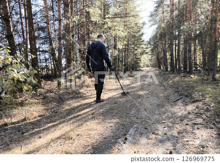 A man treasure hunter with a metal detector in the forest. Treasure hunter on a mission exploring the forest with a metal detector in search of lost history and hidden gems. 126969775