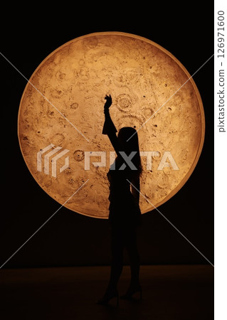 A Silhouetted Figure Standing Majestically Against a Large and Glowing Celestial Orb 126971600