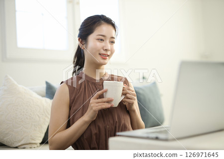 一位二十多歲的女士在客廳裡用筆記型電腦工作 126971645