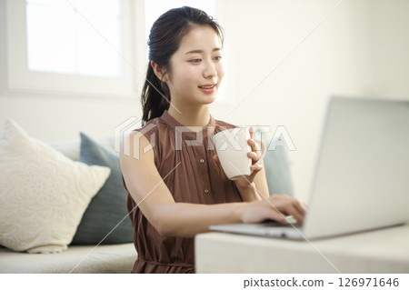 一位二十多歲的女士在客廳裡用筆記型電腦工作 一位二十多歲的女士在客廳裡用筆記型電腦工作 126971646