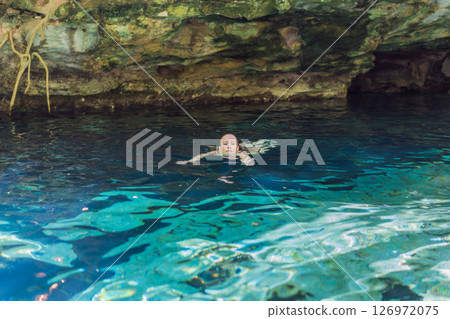 Female tourist enjoying a refreshing swim in a Mexican cenote with turquoise water. Adventure, travel, and nature exploration concept 126972075