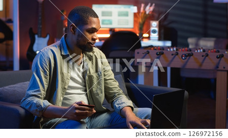 Young guy managing online banking and payments with the credit card, entering digits on website to confirm and oversee money transfer. Casual woman at home makes transactions. Camera B. 126972156