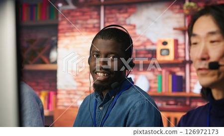Portrait of smiling technical support specialist in call center office doing troubleshooting. Upbeat african american IT worker fixing customer connectivity issue, using headphones, camera A Portrait of smiling technical support specialist in call center office doing troubleshooting. Upbeat african american IT worker fixing customer connectivity issue, using headphones, camera A 126972173
