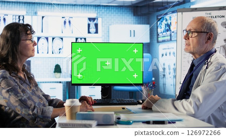 Old general practitioner discusses with female patient next to green screen, offering details from the recovery plan at the medical appointment. Medic consulting woman in cabinet. Camera B. Old general practitioner discusses with female patient next to green screen, offering details from the recovery plan at the medical appointment. Medic consulting woman in cabinet. Camera B. 126972266