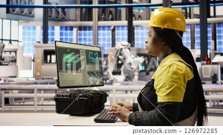 Engineer in photovoltaics factory using PC display to look at system performance metrics. Worker in industry 4.0 plant using computer screen to track energy production through IoT sensors, camera A Engineer in photovoltaics factory using PC display to look at system performance metrics. Worker in industry 4.0 plant using computer screen to track energy production through IoT sensors, camera A 126972285