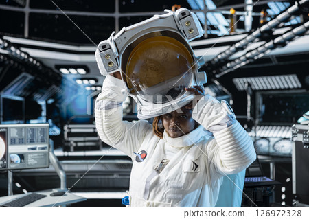 Portrait of female cosmonaut putting on cosmic gear helmet, preparing for planetary mission outside. African american woman in orbital station beginning landing procedures on solar system planet Portrait of female cosmonaut putting on cosmic gear helmet, preparing for planetary mission outside. African american woman in orbital station beginning landing procedures on solar system planet 126972328