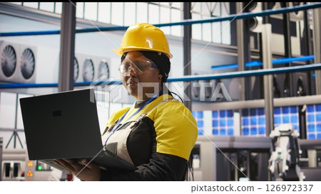 Woman working in industry 4.0 plant using notebook, following maintenance procedures. Smart factory staff member analyzing data on laptop to predict gear failures, camera A 126972337