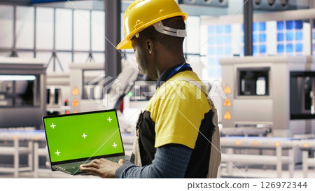Engineer in smart factory using green screen laptop to analyze IoT sensors data. Industry 4.0 plant expert performing system diagnostics on chroma key mockup notebook to reduce downtime, camera B Engineer in smart factory using green screen laptop to analyze IoT sensors data. Industry 4.0 plant expert performing system diagnostics on chroma key mockup notebook to reduce downtime, camera B 126972344