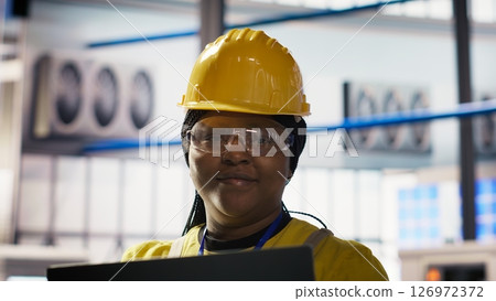 Smiling smart factory specialist testing automated systems to ensure reliability. Happy engineer in industry 4.0 industrial plant identifying bottlenecks and optimizing gear based on data, camera B 126972372