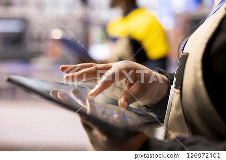 Smart factory engineer using a tablet to develop production line layouts in CAD software. Close up of african american worker optimizing industrial floor configurations with digital tool. Smart factory engineer using a tablet to develop production line layouts in CAD software. Close up of african american worker optimizing industrial floor configurations with digital tool. 126972401