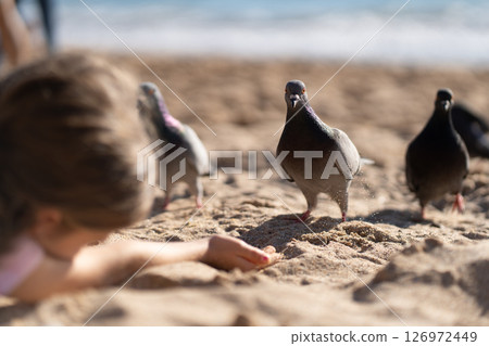 Girl extending hand to feed doves on sandy beach 126972449