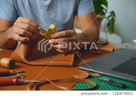 Leather craftsman gluing lining to brown leather bag in workshop 126973601