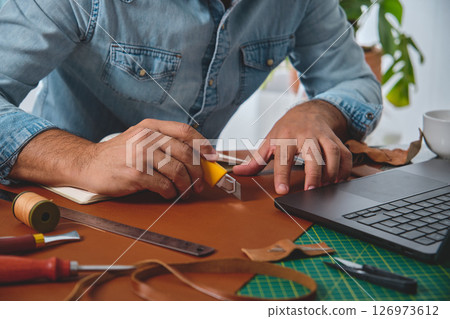 Leather craftsman cutting leather with cutter in workshop 126973612