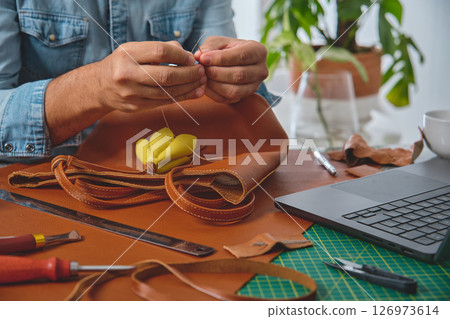 Leather craftsman sewing a bag in his workshop Leather craftsman sewing a bag in his workshop 126973614