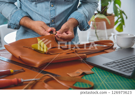 Leather craftsman attaching strap to handmade bag in workshop 126973623