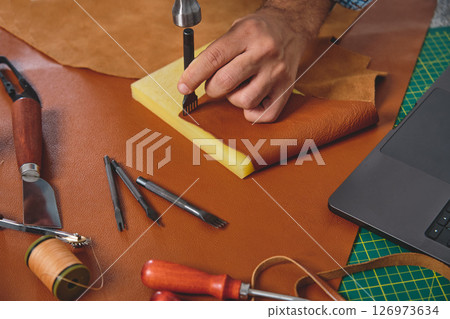 Shoemaker working leather with hammer and punching tool in workshop 126973634