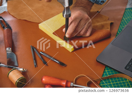 Shoemaker working leather with hammer and punching tool in workshop Shoemaker working leather with hammer and punching tool in workshop 126973636
