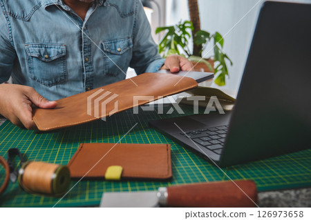 Craftsman putting laptop into handmade leather case in his workshop Craftsman putting laptop into handmade leather case in his workshop 126973658