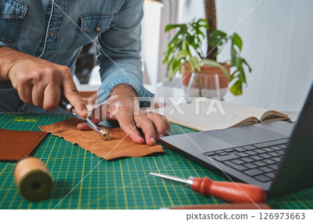 Shoemaker working leather at home with laptop and tools 126973663