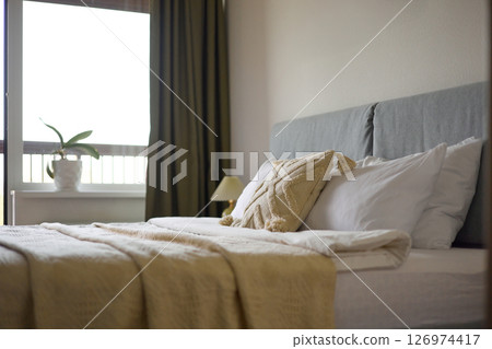 Cozy bedroom interior, beige bedspread and pillow, bedside lamp next to the bed, light from the window Cozy bedroom interior, beige bedspread and pillow, bedside lamp next to the bed, light from the window 126974417