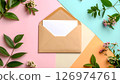 Blank white card in a brown envelope with green leaves and pink flowers on a colorful background. 126974761