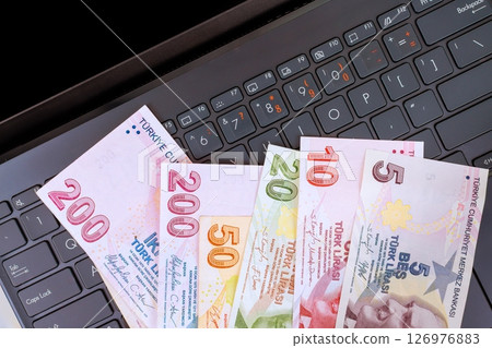 Various denominations Turkish lira banknotes on laptop highlight finance digital transactions in workspace. 126976883