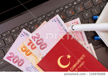 Currency lira banknotes, Turkey passport lie on laptop keyboard, indicating travel planning financial readiness. Currency lira banknotes, Turkey passport lie on laptop keyboard, indicating travel planning financial readiness. 126976886