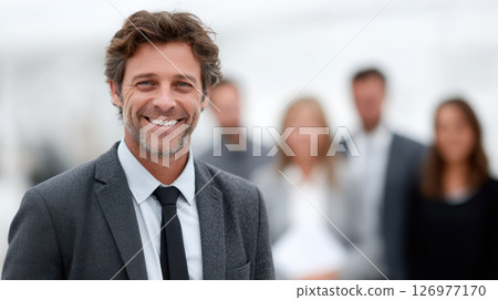 Confident businessman suit tie smiling standing office blurred colleagues professional team 126977170