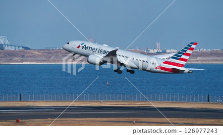An American passenger plane taking off from runway C at Haneda Airport stands out against the Tokyo Bay skyline. 126977243