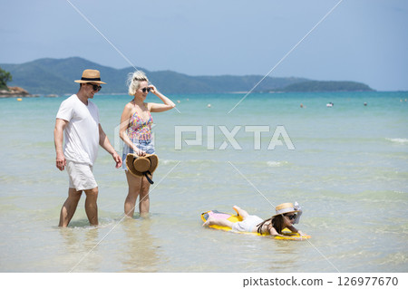 Happy family relax walking on beach with daughter on surfboard. Joyful vacation with parents and children at the sea Trip enjoying bonding. together. 126977670