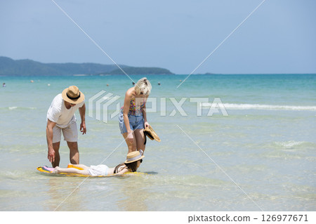 Happy family relax walking on beach with daughter on surfboard. Joyful vacation with parents and children at the sea Trip enjoying bonding. together. 126977671