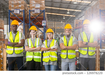 Full teamwork of warehouse employees wear yellow hard hat standing with surrounded shelves in warehouse. Portrait team professional worker safety uniform crossed arms looking at camera. 126978220