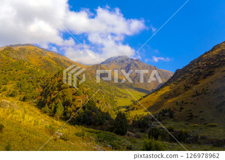 Dramatic mountain valley with steep slopes, patches of vegetation, and a cloudy blue sky. Dramatic mountain valley with steep slopes, patches of vegetation, and a cloudy blue sky. 126978962