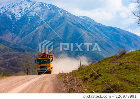 Yellow concrete boom pump truck driving on a dusty mountain road. 126978991