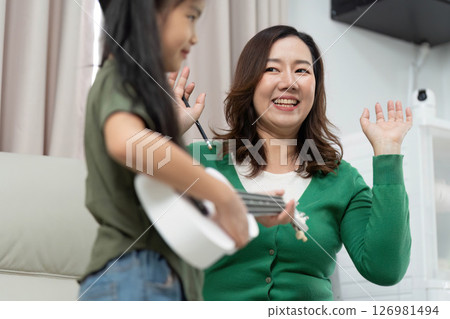 Music Education and Joyful Learning. A mother encouraging her daughter during a music lesson at home. Music Education and Joyful Learning. A mother encouraging her daughter during a music lesson at home. 126981494