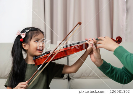 Musical Bonding. A joyful child learning violin with mother at home. 126981502