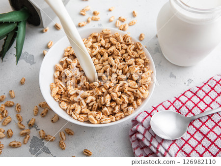 Pouring milk in to bowl with honey rice krispies morning cereal breakfast with spoon and kitchen Pouring milk in to bowl with honey rice krispies morning cereal breakfast with spoon and kitchen 126982110