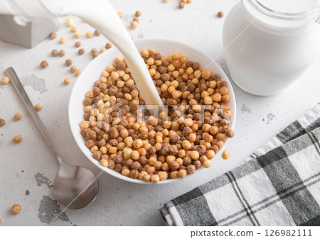 Milk pouring in to bowl with mini peanut butter puffs cereal morning breakfast with spoon Milk pouring in to bowl with mini peanut butter puffs cereal morning breakfast with spoon 126982111
