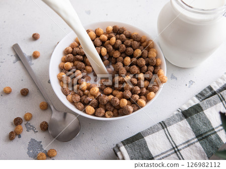 Milk pouring in to bowl with healthy peanut butter puffs cereal morning breakfast with spoon Milk pouring in to bowl with healthy peanut butter puffs cereal morning breakfast with spoon 126982112
