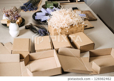 Empty kraft boxes arranged near shredded filler and handmade soaps in a clean workspace. Scalable packaging, modular box system, ecommerce adaptability, compact packaging trend 126982462